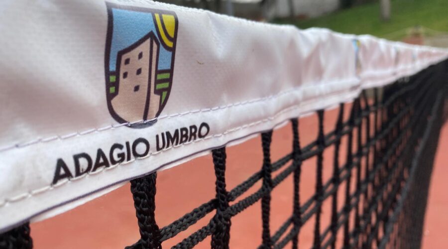 Tennis net with Adagio Umbro logo, set against the scenic backdrop of the tennis court in Umbria, Italy.